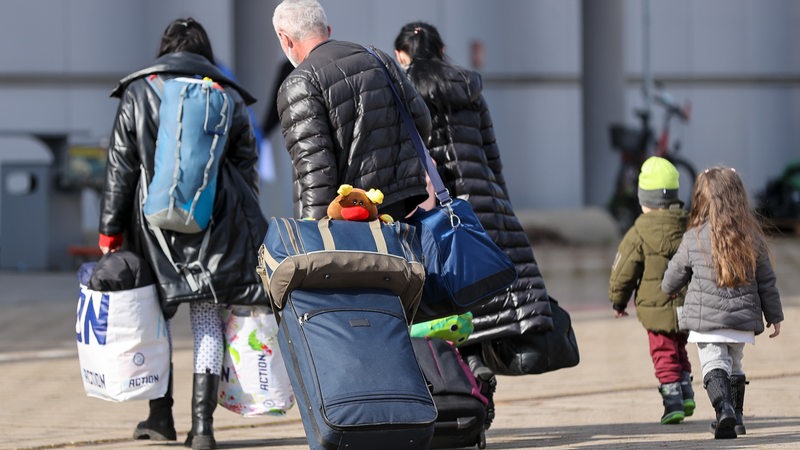 Mehre Erwachsene und Kinder laufen mit Gepäck.