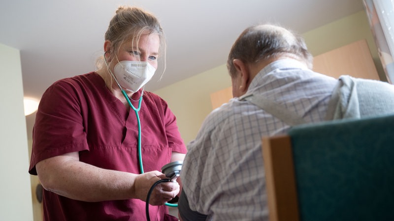 Pflegerin mit Corona-Maske misst Blutdruck