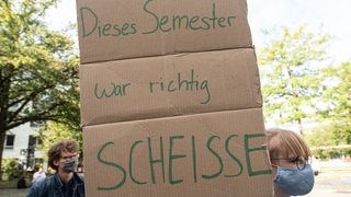 Eine Studentin hält ein Plakat mit der Aufschrift "Dieses Semester war richtig scheiße" hoch