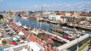 Blick von oben auf ein Hafenbecken mit vielen Schiffen und Menschen.