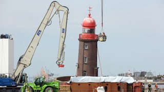 Experten schauen sich bei einer Inspektion von einem Korb aus den schiefen Leuchtturm auf der Mole in Bremerhaven an. 