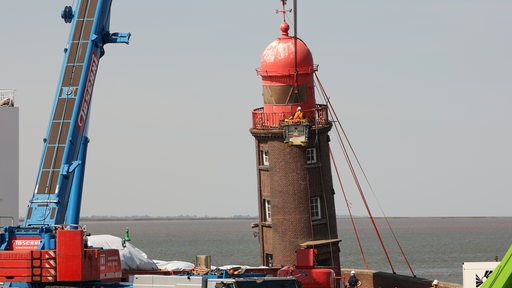 Von einer Krangondel aus wird am schiefen Leuchtturm auf der Mole in Bremerhaven die Demontage der Kuppel vorbereitet.