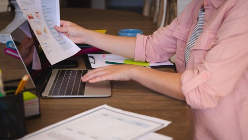 Eine junge Frau arbeitet mit Papieren am Laptop.