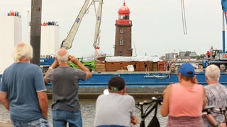 Zuschauer verfolgen die Arbeiten an dem schiefen Leuchtturm auf der Mole in Bremerhaven. 