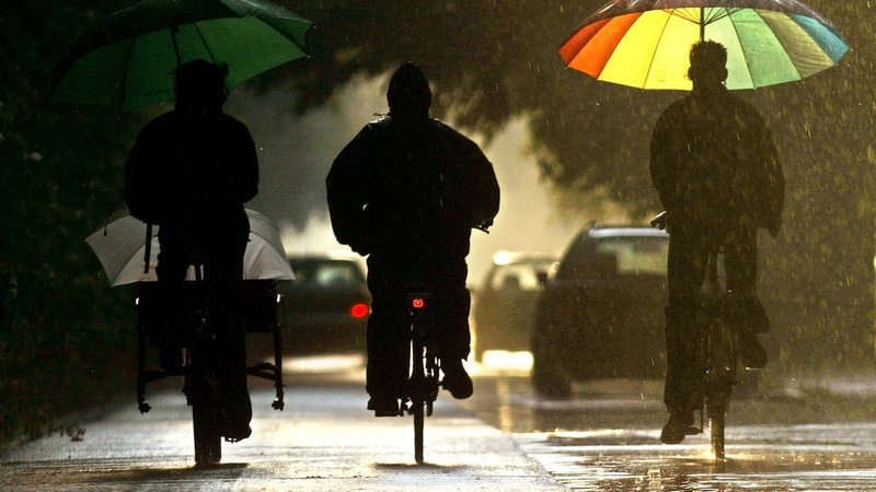 Drei Radfahrer fahren in Bremen durch schweren Gewitterregen in die Abendsonne. 