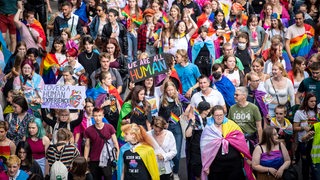 Mit umgehängten Regenbogenfahnen ziehen Menschen beim Christopher Street Day (CSD) Bremen durch die Innenstadt.