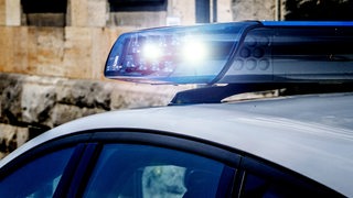 Ein Polizeiauto steht vor einer Hauswand, das Blaulicht blinkt.