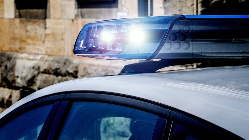 Ein Polizeiauto steht vor einer Hauswand, das Blaulicht blinkt.