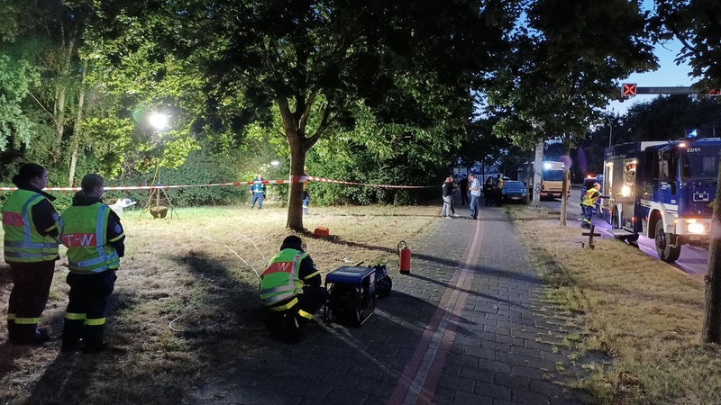 Polizisten stehen auf einer abgesperrten Rasenfläche. Am Straßenrand stehen Einsatzfahrzeuge. Ein Passant hat am Montag in Bremerhaven im Ortsteil Geestemünde unweit des Flusses Geeste einen Leichnam entdeckt. Die Kriminalpolizei hat die Ermittlungen aufgenommen.
