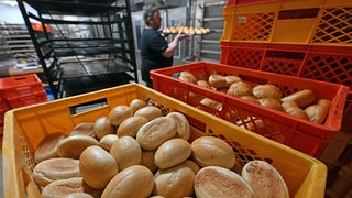 Ein Mann holt  Brötchen aus dem Ofen einer Backstube