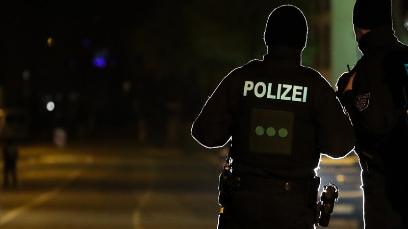 Polizisten aus Niedersachsen überwachen bei Dunkelheit im Gegenlicht eine Zufahrtsstraße in Chemnitz. 
