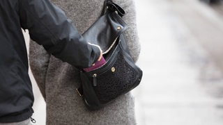 Nahaufnahme einer Person, die einer Frau das Portemonnaie aus der Handstasche stiehlt