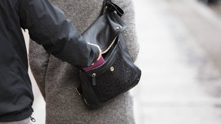 Nahaufnahme einer Person, die einer Frau das Portemonnaie aus der Handstasche stiehlt
