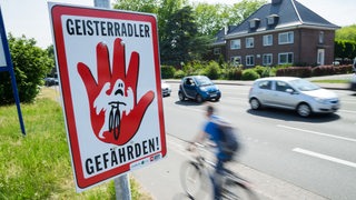 Ein Fahrradfahrer fährt zwischen einem Schild und Autos hindurch.