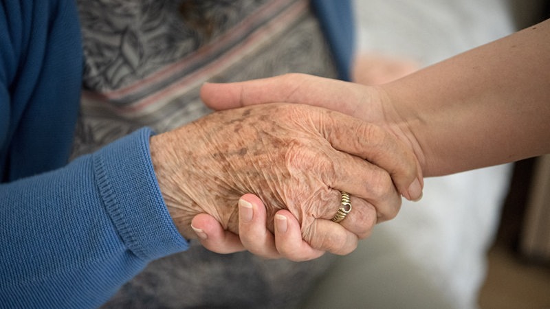 Eine Pflegefachkraft hält die Hand einer Bewohnerin des Seniorenheims.