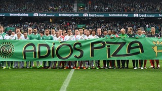 Claudio Pizarro und alle Spieler seiner drei Teams halten auf dem Rasen ein großes Banner mit der Aufschrift "Adios Piza" hoch.