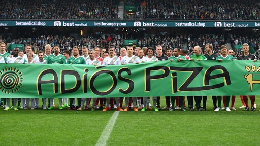 Claudio Pizarro und alle Spieler seiner drei Teams halten auf dem Rasen ein großes Banner mit der Aufschrift "Adios Piza" hoch.