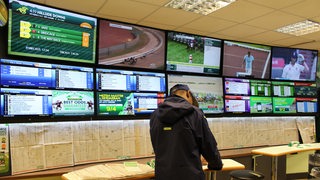 Ein Mann steht in einem Wettbüro vor vielen Bildschirmen mit Sportübertragungen