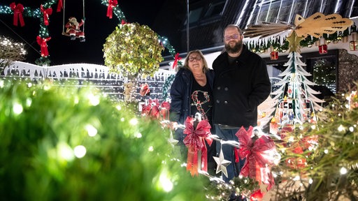 Eine Frau und ein Mann stehen vor einem weihnachtlich beleuchteten Haus