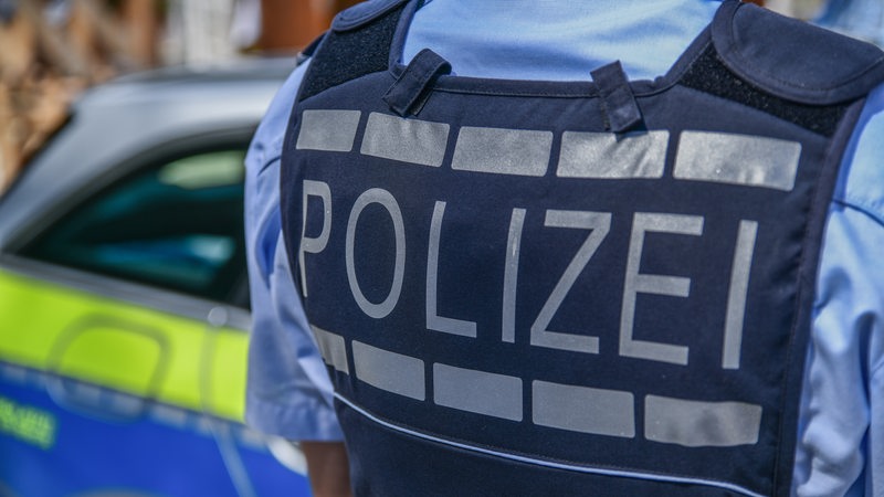Polizist steht mit Rücken zur Kamera vor Polizeiauto