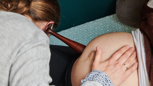 Eine Hebamme hört den Bauch einer schwangeren Frau ab