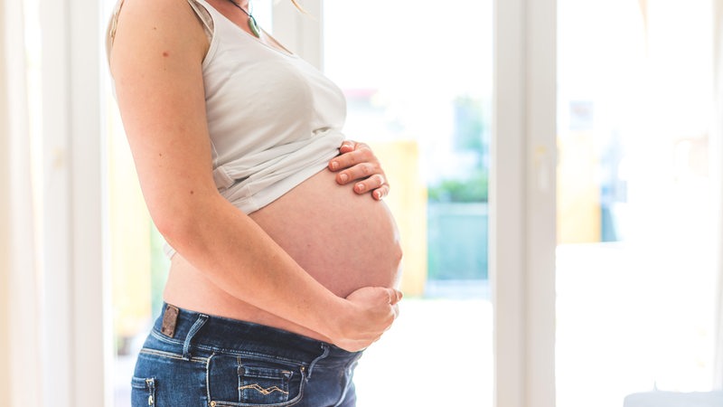 Eine schwangere junge Frau umfasst ihren Bauch.