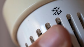Eine Hand regelt das Thermostat einer Heizung.