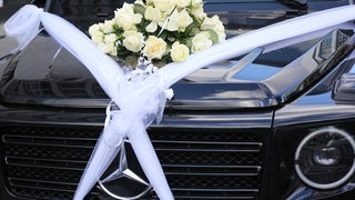 Ein großer Geländewagen steht geschmückt mit weißen Schleifen und Rosen bereit für einen Hochzeitskorso.