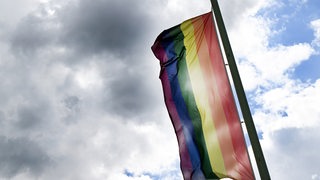 Eine Regenbogenfahne vor einem bewölkten Himmel.