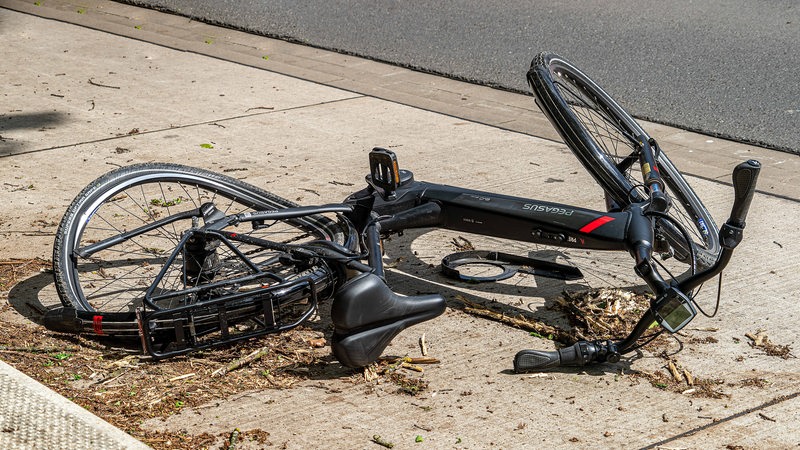 Ein Elektrofahrrad liegt nach einem Unfall stark beschädigt an einer Strasse. 