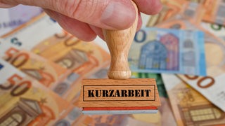 Eine Hand hält einen Stempel auf dem "Kurzarbeit" steht.