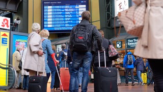Zahlreiche Reisende vor einer Anzeigetafel mit An- und Abfahrtszeiten der Züge am Hamburger Hauptbahnhof. 