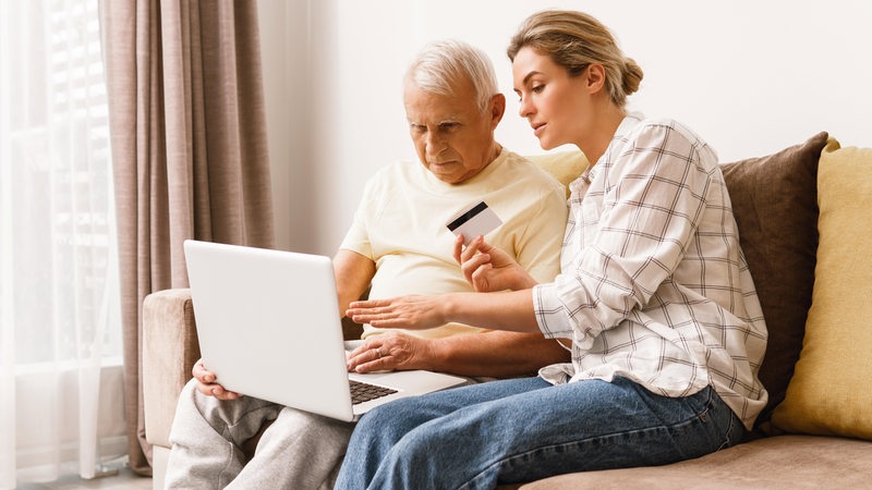 Eine junge Frau zeigt einem Senioren, wie das Online-Banking funktioniert