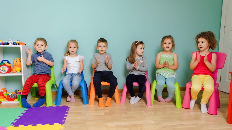 Kinder sitzen auf bunten Stühlen und klatschen