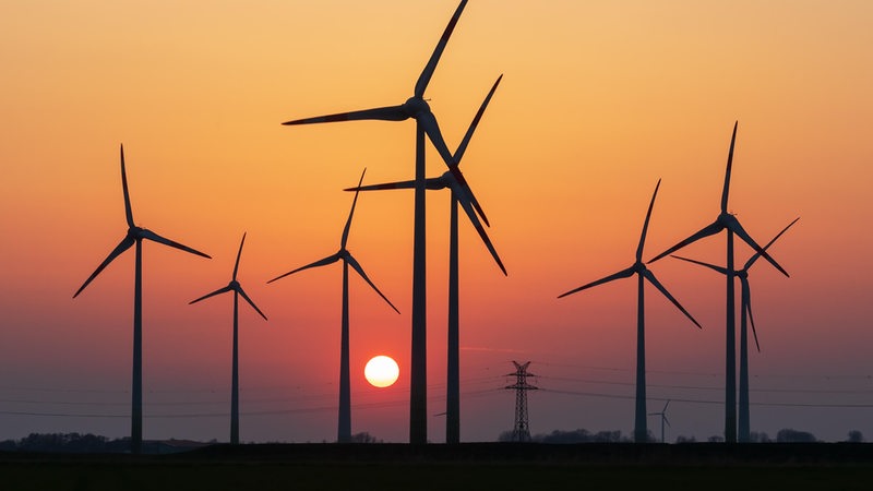 Hinter Windrädern geht die Sonne unter.