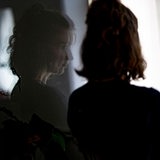 Eine Frau steht in ihrer Wohnung an einem Fenster. 