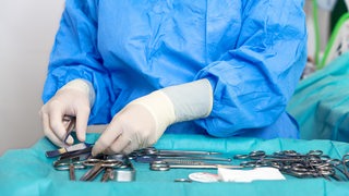 Ein OP-Mitarbeiter sortiert das Chirurgie-Besteck bestehend aus Scheren.
