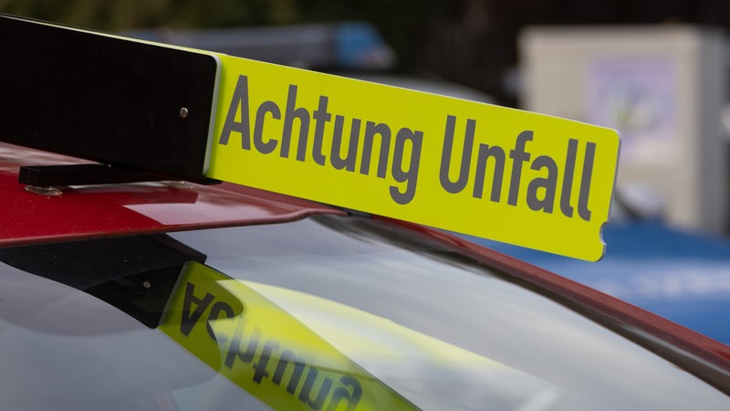 Auf einem roten Einsatzfahrzeug steht ein Schild mit der Aufschrift "Achtung Unfall".