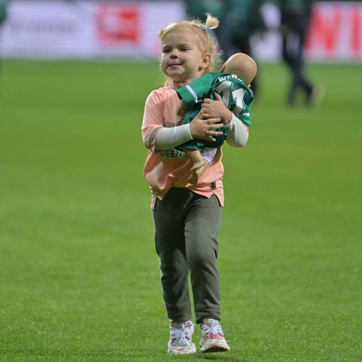 Die kleine Tochter von Niclas Füllkrug im Trikot mit ihrer Puppe auf dem Arm auf dem Rasen des Weser-Stadions, nachdem sie Einlaufkind mit Papa war.