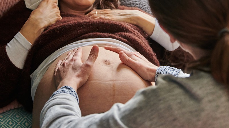 Eine Hebamme tastet in ihrer Praxis den Bauch einer schwangeren Frau ab.