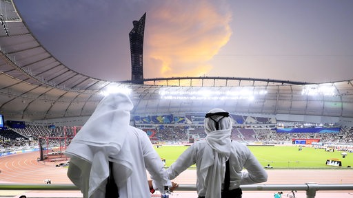 Zwei Männer sehen vom Zuschauer-Rang in das Fussball-Station der WM 2022 Katar