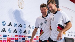 Die Nationalspieler Thomas Müller und Niclas Füllkrug verlassen Arm in Arm lächelnd das Podium der Pressekonferenz.