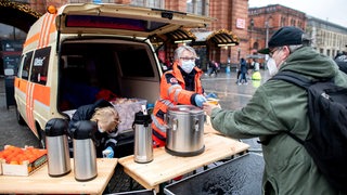 Karin Stelljes, Teamleiterin beim Kältebus der Johanniter, reicht an Heiligabend auf dem Vorplatz am Hauptbahnhof eine warme Mahlzeit an einen bedürftigen Menschen.