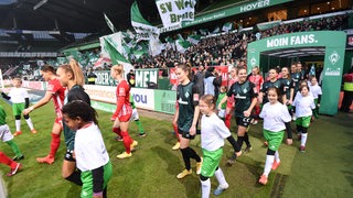 Werders Fußballerinnen kommen mit Einlaufkindern an der Hand aus dem Spielertunnel im Weser-Stadion.