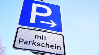 Ein Schild mit der Aufschrift "mit Parkschein" steht an einem Parkplatz.