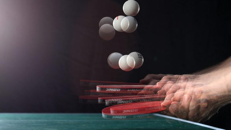 Ein Tischtennisball wird mit einem Schläger hochgespielt, durch Mehrfachbelichtung wirkt es wie acht Bälle in der Luft.