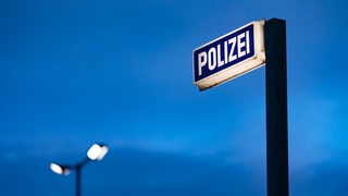 Vor einem dunklen Himmel steht ein Leuchtschild mit der AUfschrift Polizei.