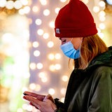 Frau mit einer Maske vor leuchtenden Weihnachtslichtern