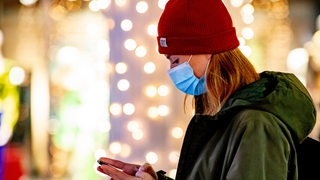 Frau mit einer Maske vor leuchtenden Weihnachtslichtern