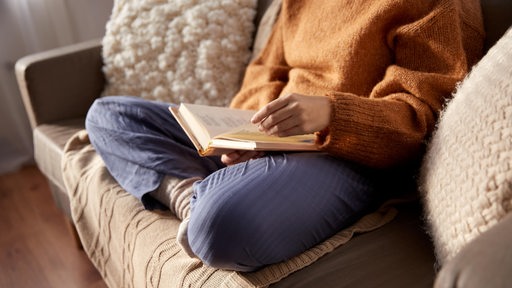 Eine Person sitzt auf einem Sofa und liest in einem Buch.